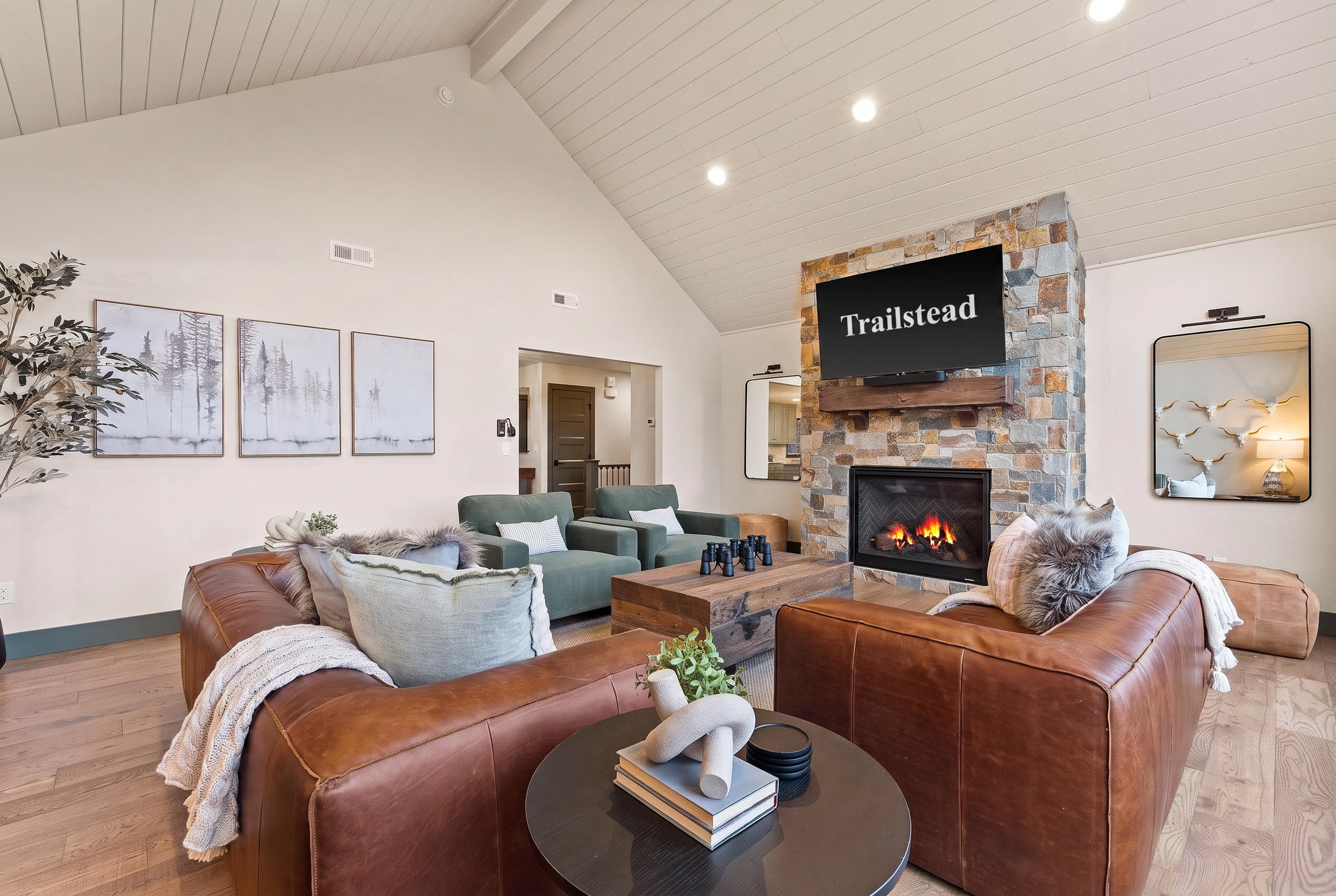 The Tamarack — living room with leather couches, green armchairs, coffee table, and a stone fireplace with tv